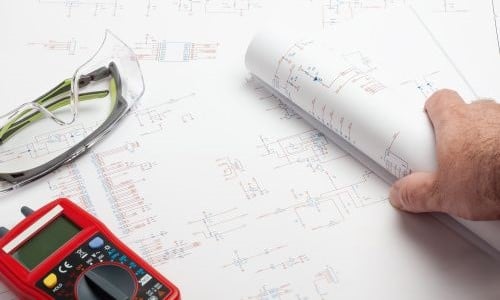 Engineer reviewing schematics with multimeter and safety glasses