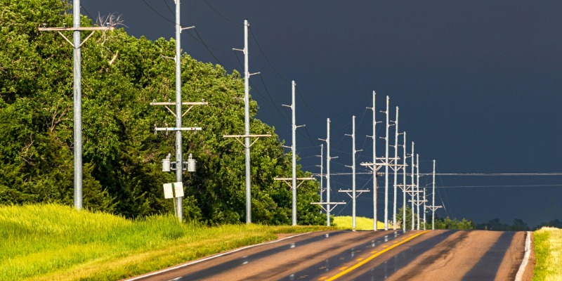 Row of silver metal power poles alongside wet Nebraska highway with dark storm clouds in the background